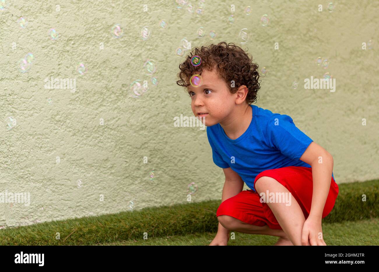curly-haired boy with freckles playing in the backyard with soap bubbles. Stock Photo