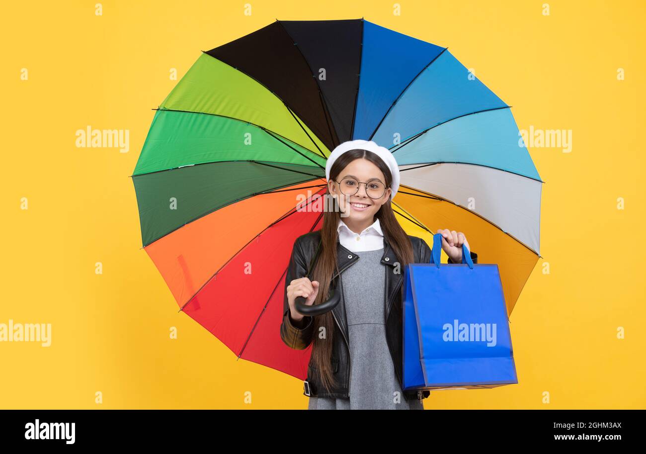 happy girl in glasses hold shopping bag. seasonal sale. teen kid under colorful parasol. Stock Photo