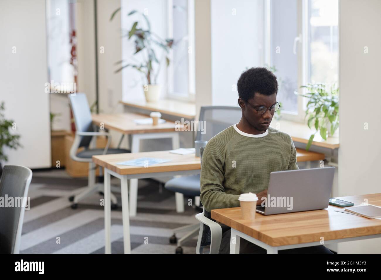 Frowning serious software developer drinking coffee and coding on laptop in open space office Stock Photo