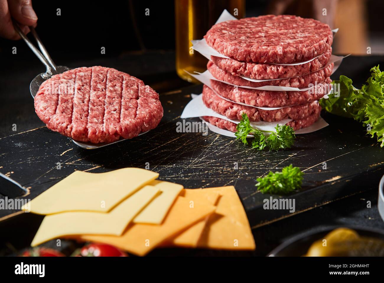 Freshly prepared ground beef burger patty on a spatula surrounded by ingredients and additional