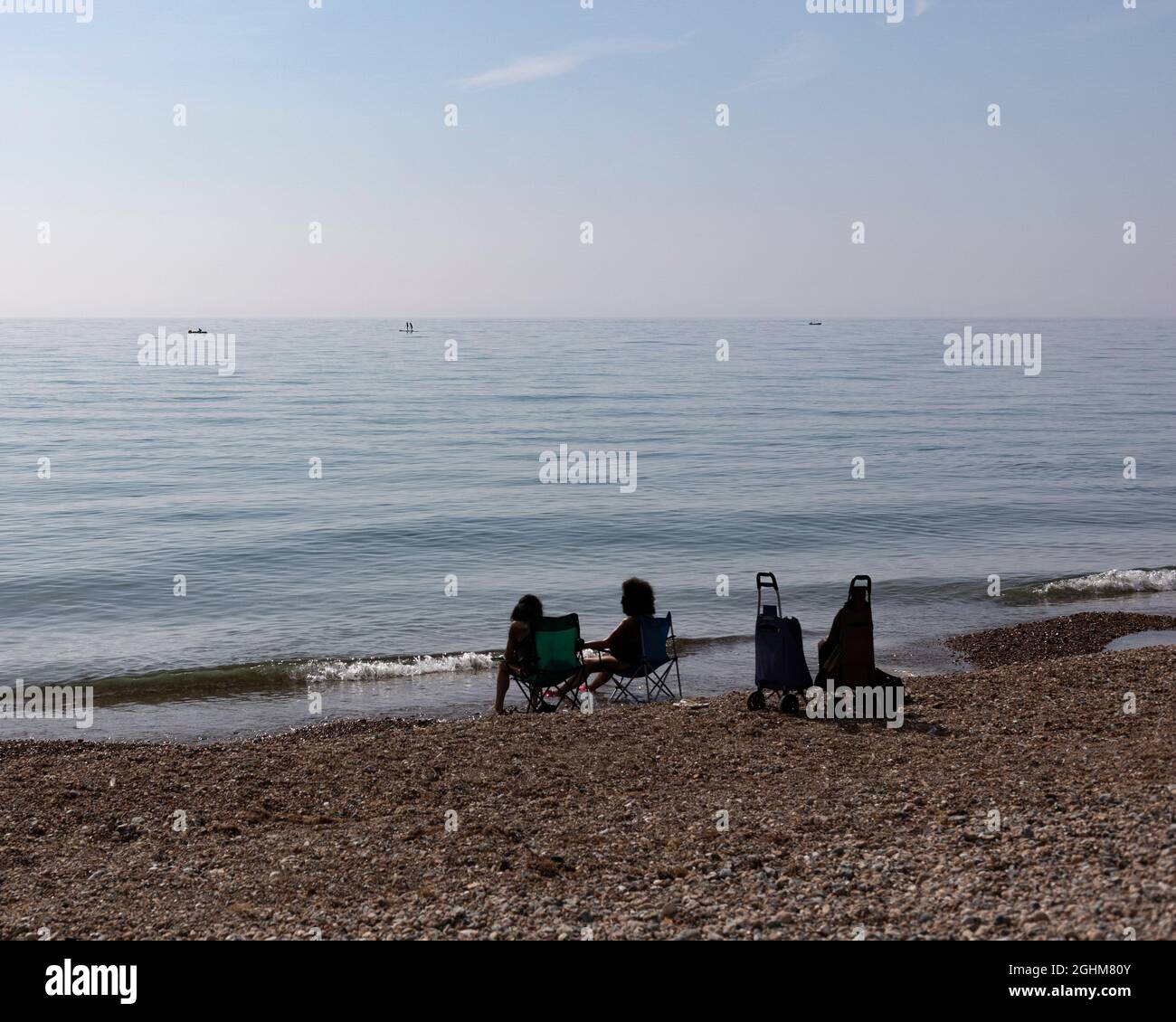 two unrecognisable ladies sitting by the sea, cooling their feet in the water, Worthing, West Sussex, UK, September 2021 Stock Photo