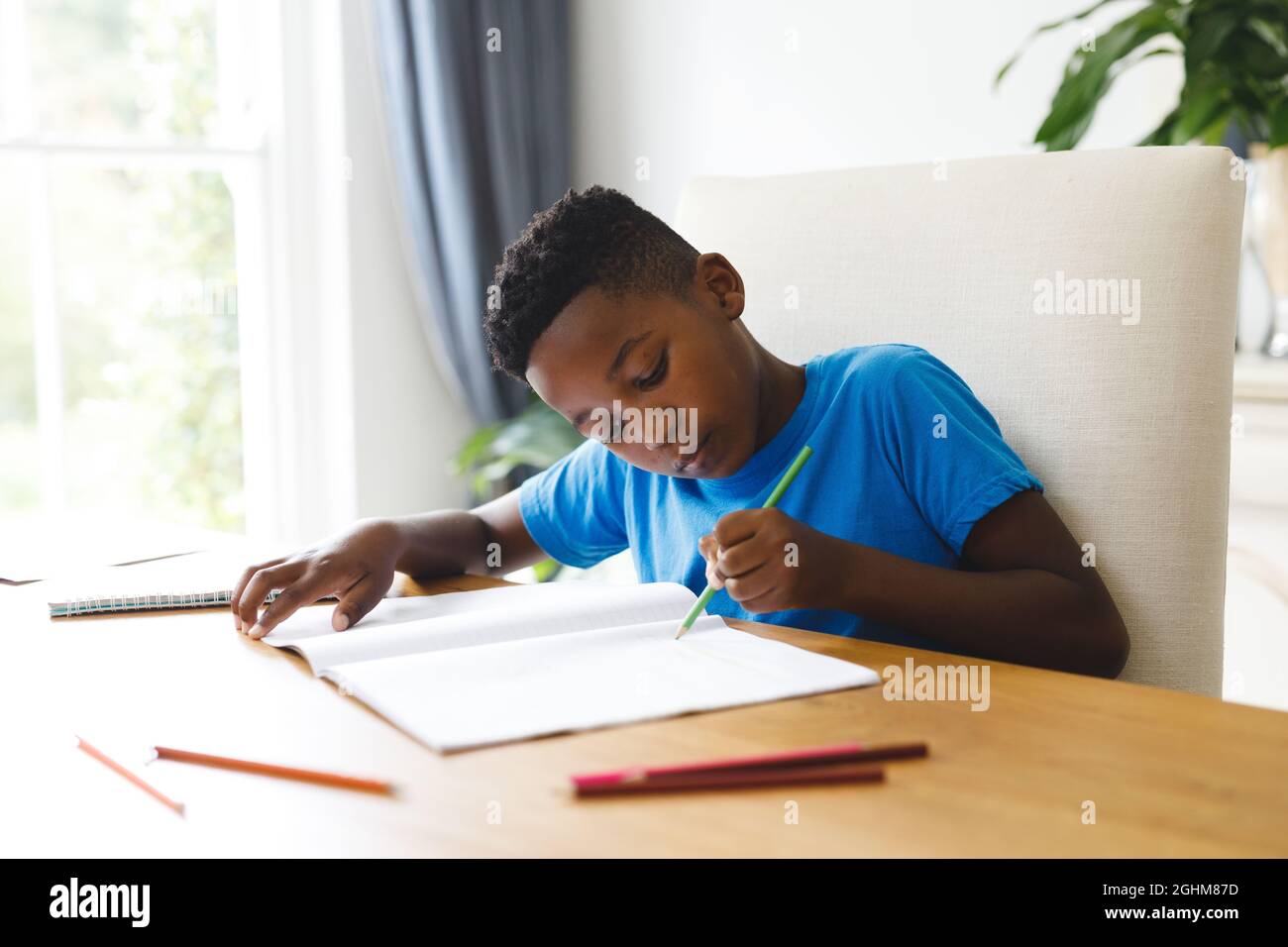 African american boy sitting at table in living room, doing homework