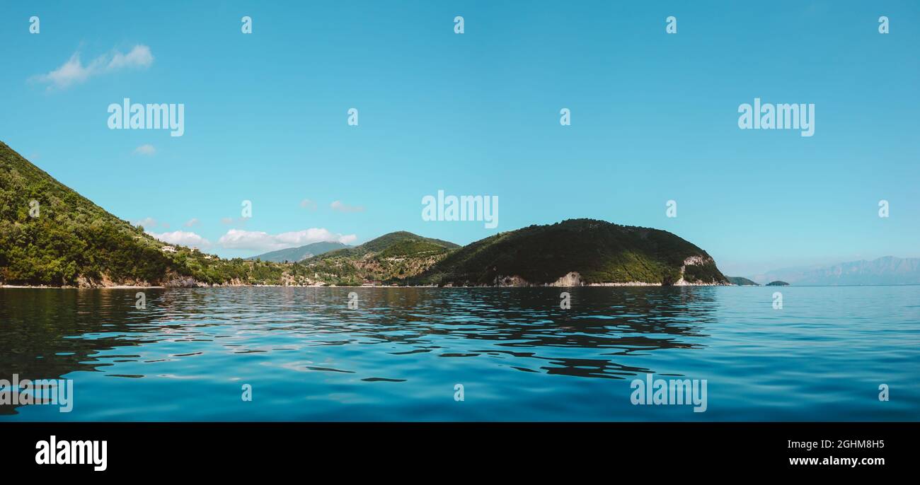 Blue clear calm Ionian Sea panorama. Water with nice reflection and scenic green hills coast. Nature of Lefkada island in Greece. Summer vacation idyl Stock Photo