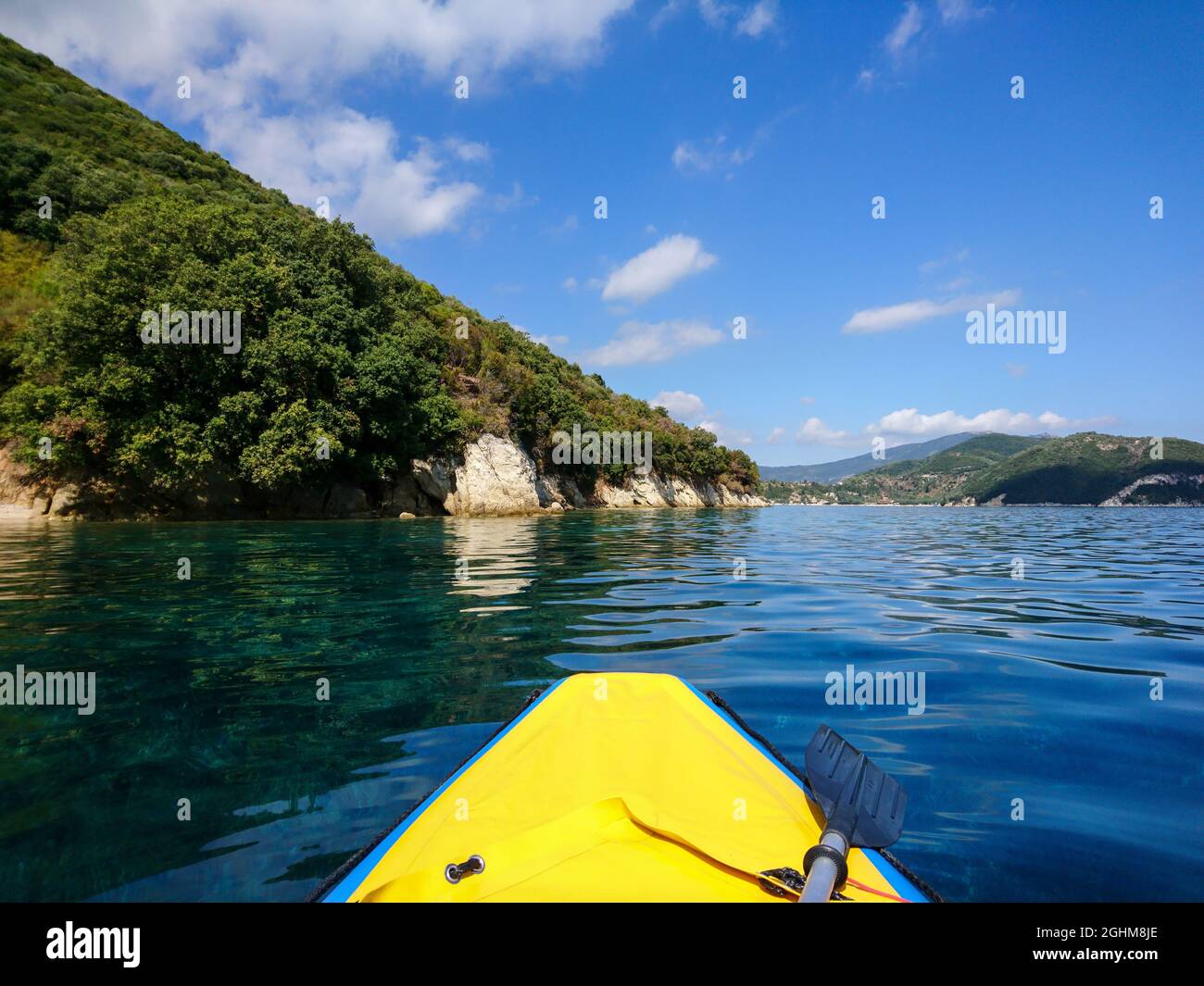 Yellow boat nose and paddle on blue clear calm Ionian Sea bay, view from boat. Nice clouds reflection and scenic green hills coast. Lefkada island in Stock Photo