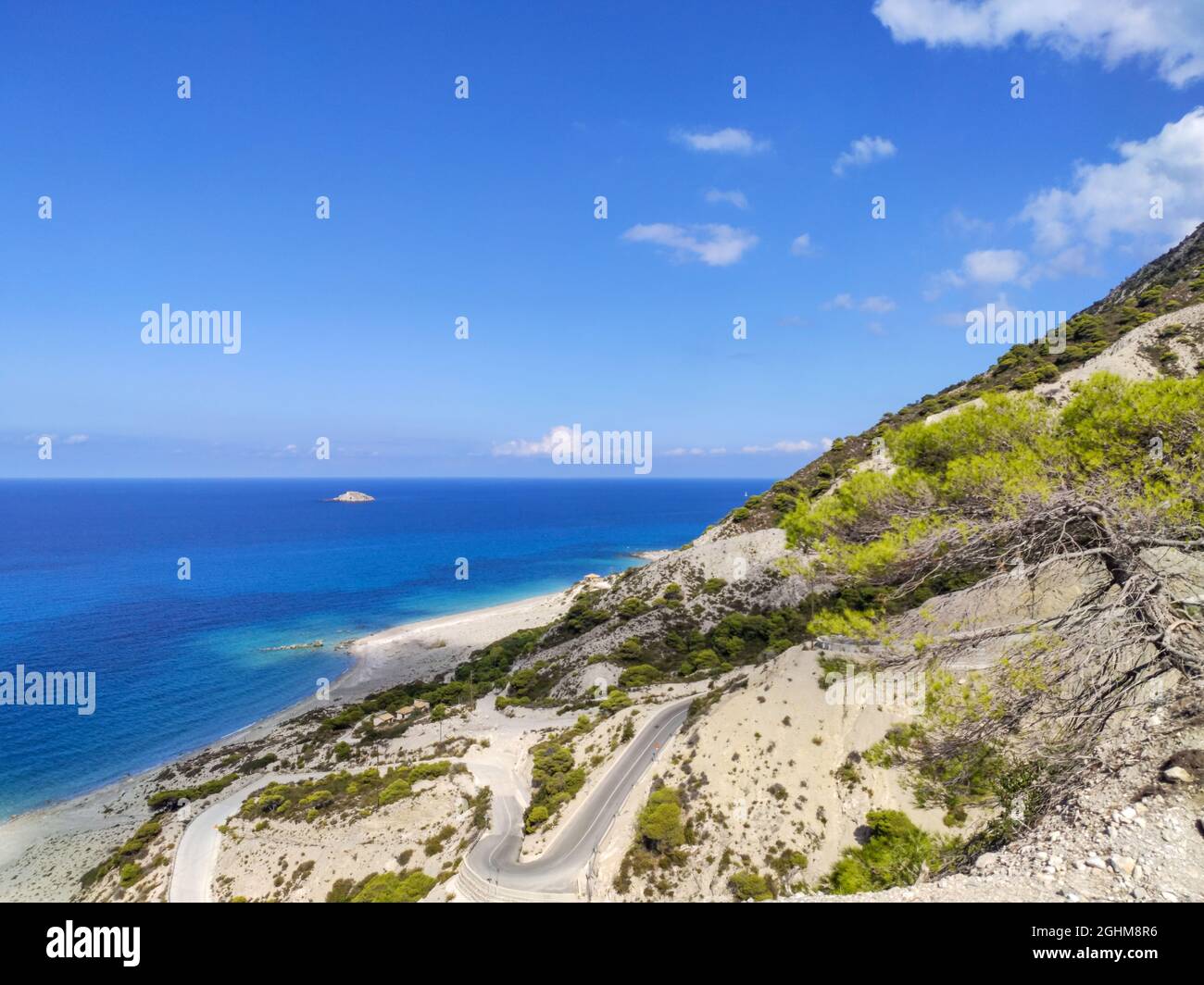 Driving mountain serpentine steep road to Gialos pebble beach with turquoise water and clear blue sky, Lefkada island, Ionian sea coast, Greece. Sunny Stock Photo