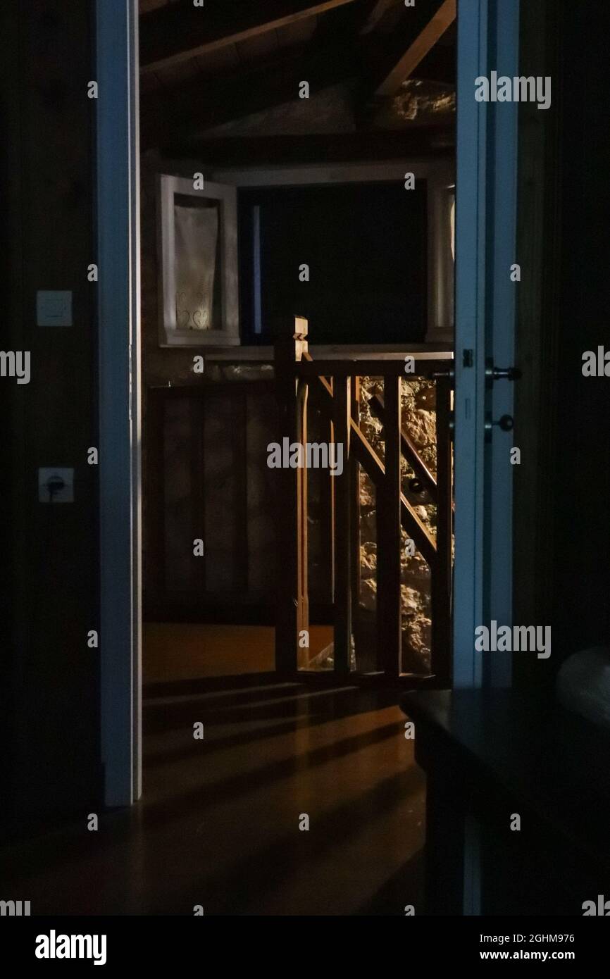 Dark second floor interior in traditional Mediterranean house. Opened doorway with stairs railings and window in night lamp light Stock Photo