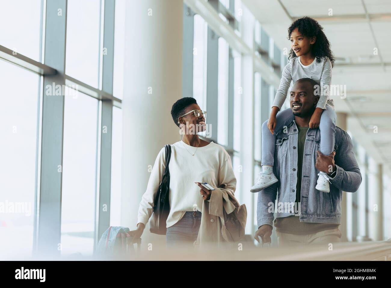 Girl on shoulder of father while walking with mother at airport. Happy family going on holiday. Stock Photo