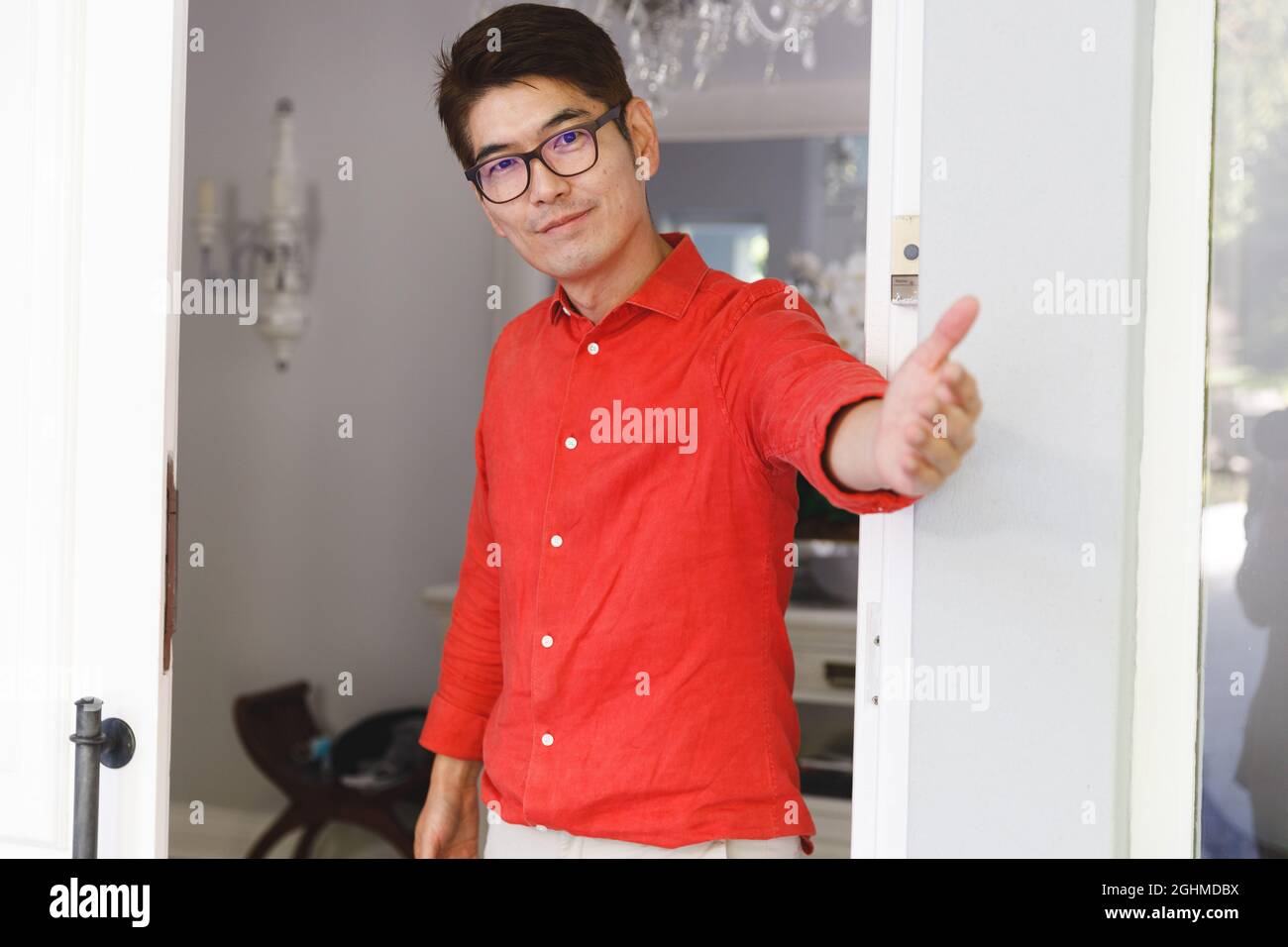 Portrait of smiling asian man standing at door and inviting visitor to room Stock Photo