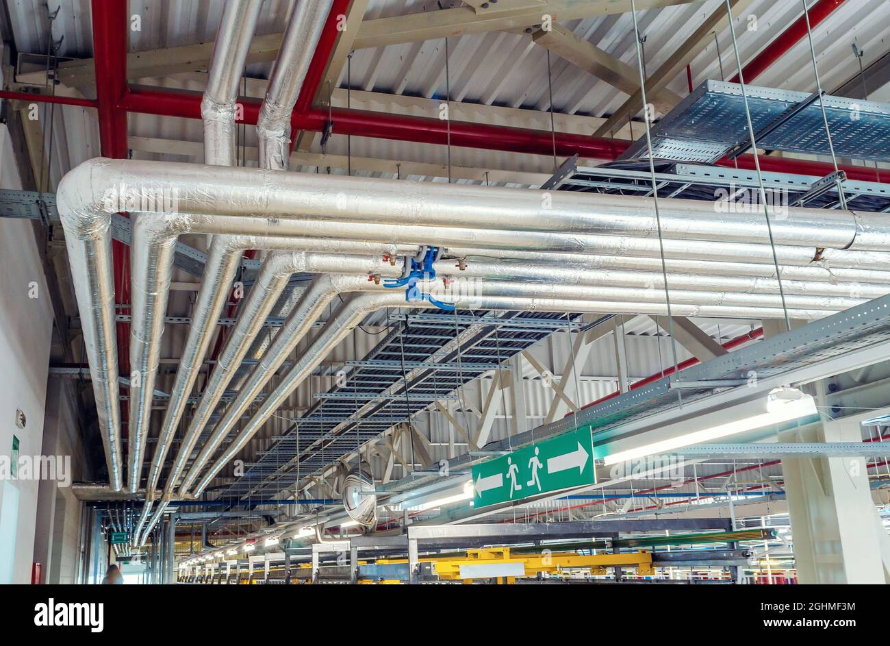 Metal pipes mounted under ceiling are covered with thermal insulation at modern production plant Stock Photo