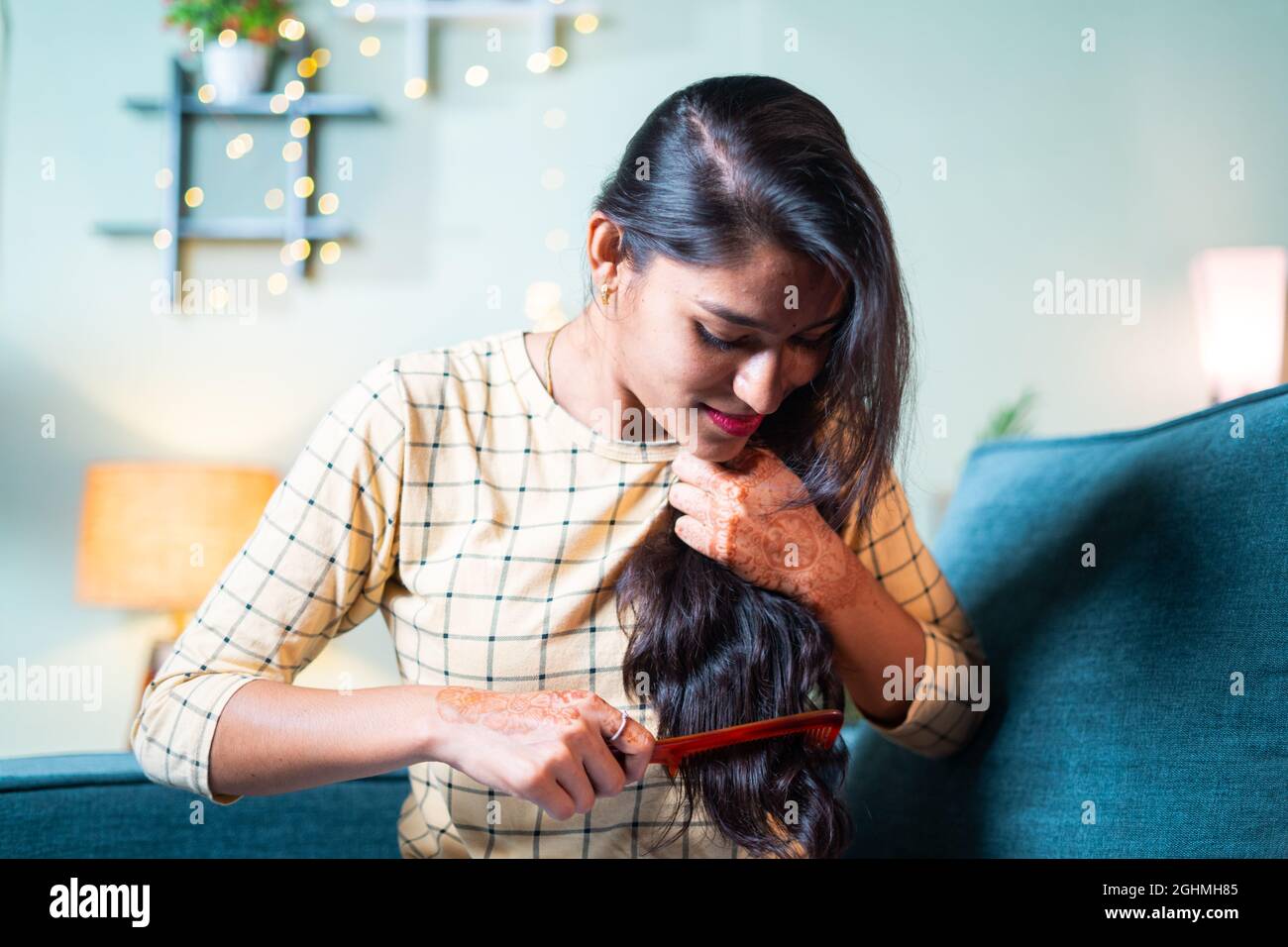 Young Indian girl on sofa combing her long hairs - concept of woman getting ready and daily rituals. Stock Photo