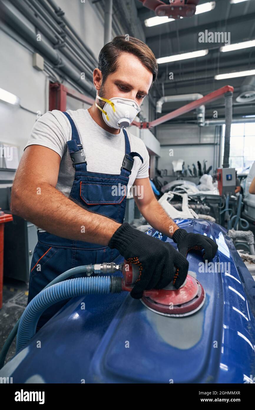 Auto mechanic in respirator using sander on car surface Stock Photo