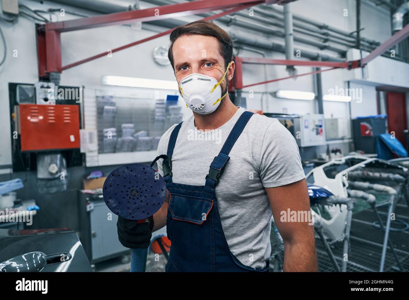 Proud auto mechanic looking at camera with sander in hand Stock Photo