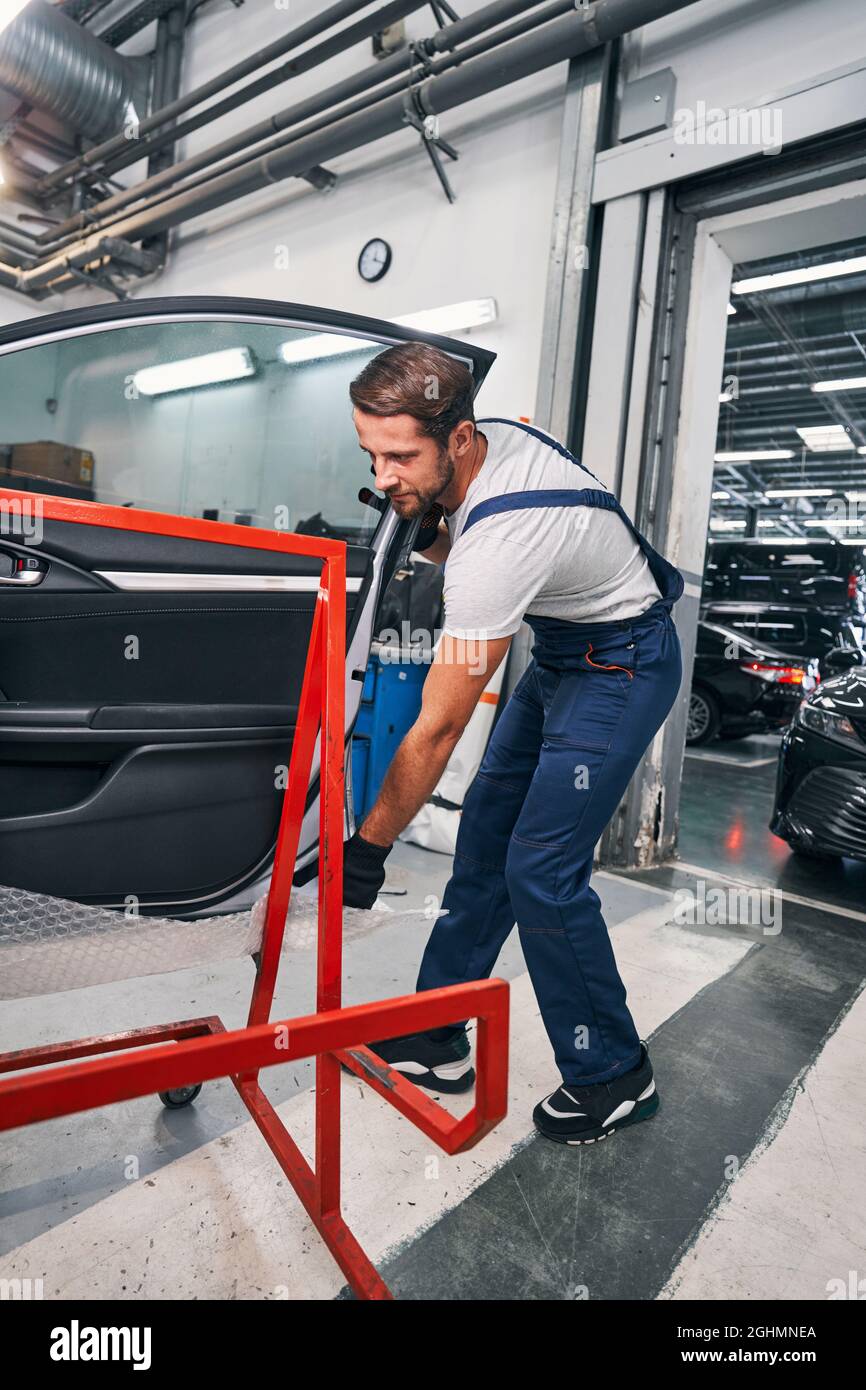 Male car service worker placing car door on red support Stock Photo
