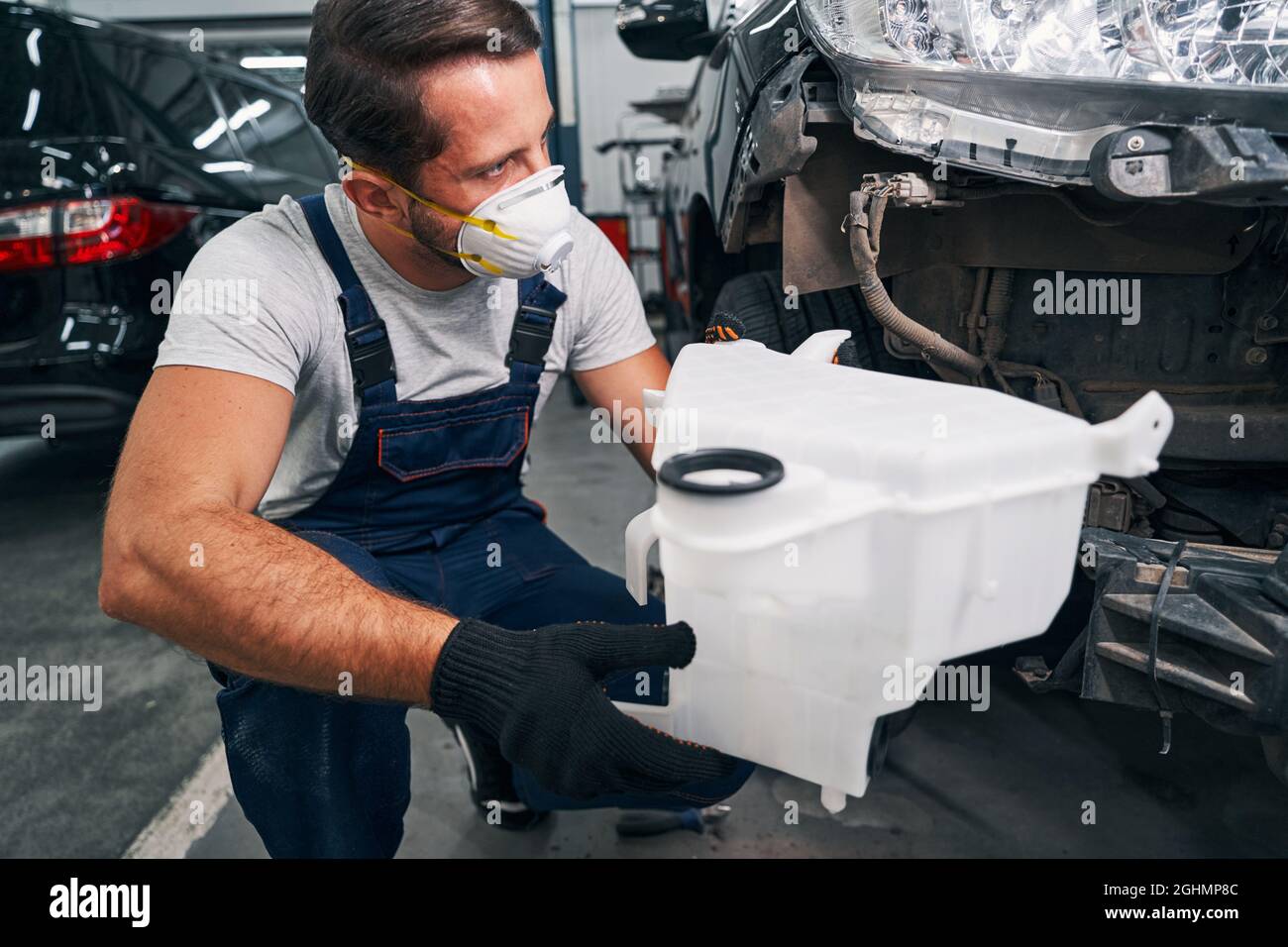Car repairman taking off washer container from auto Stock Photo