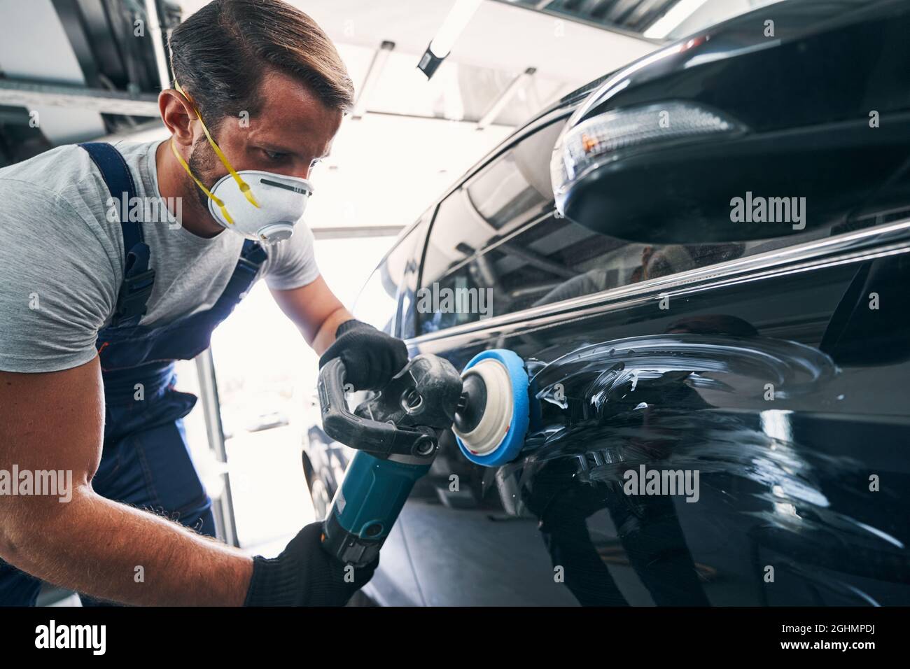 Repairman using polisher with blue pad on black automobile Stock Photo