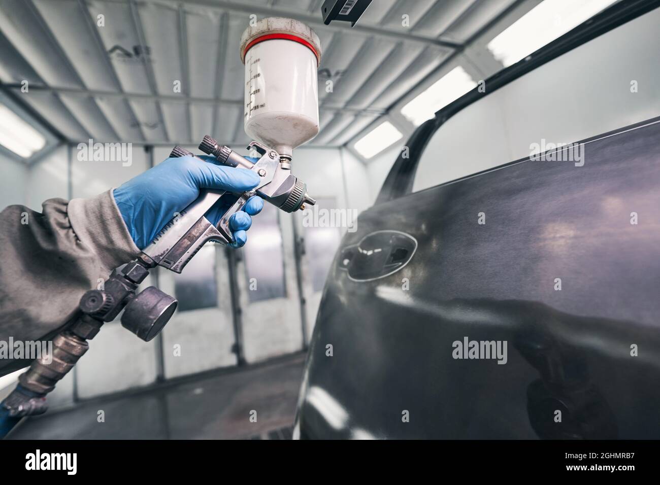 Auto workshop worker painting car door with spraying pistol Stock Photo