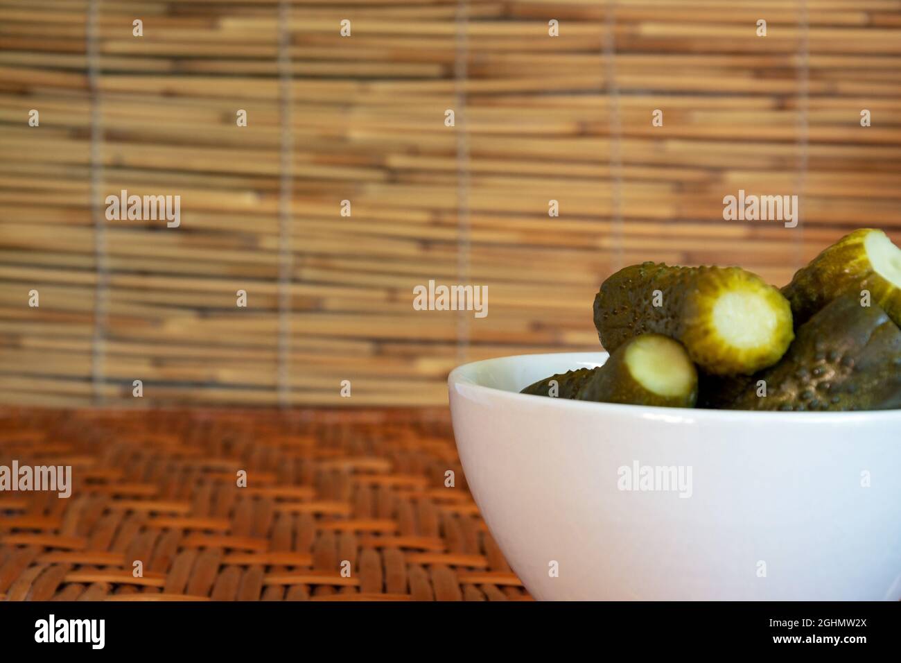 Pickles in a small deep plate of white color on a wooden table of vines and against a background of reeds. Free space. High quality photo Stock Photo