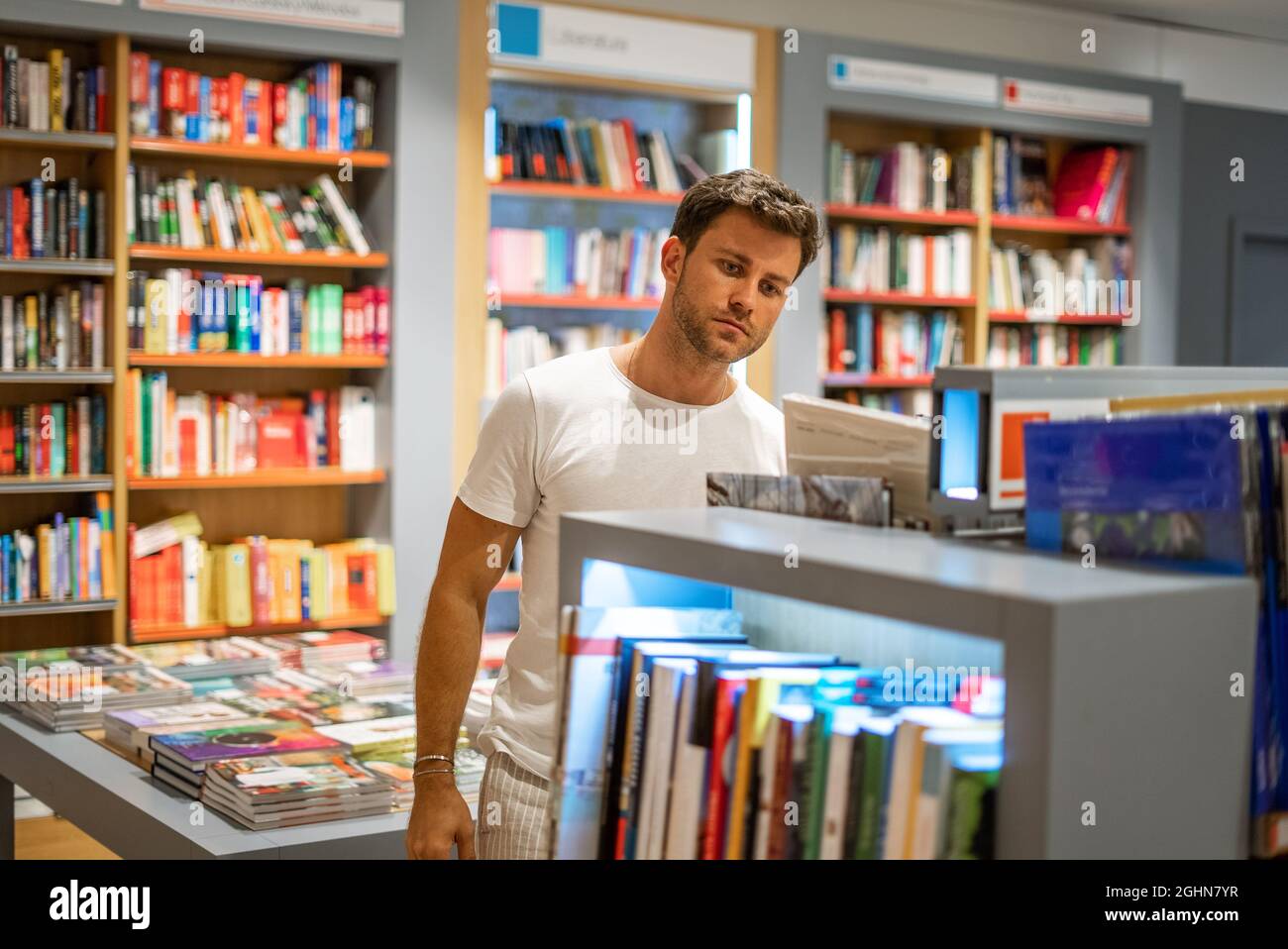 Young male buyer standing near bookcase and searching for literature while visiting modern bookshop Stock Photo