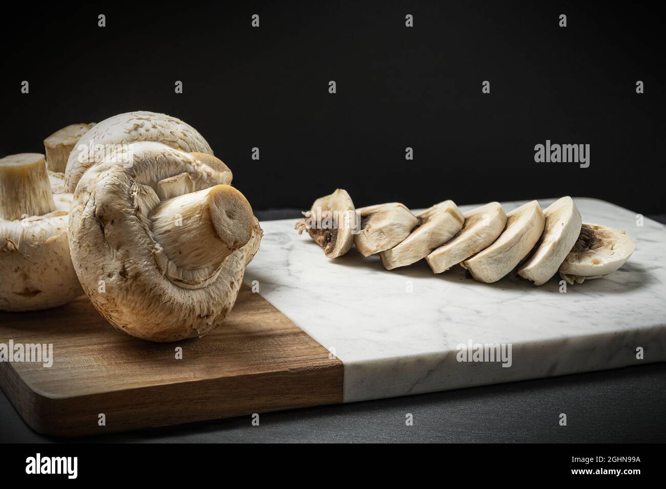 Closeup view of sliced up  champignon mushrooms and whole mushrooms on a wooden board Stock Photo