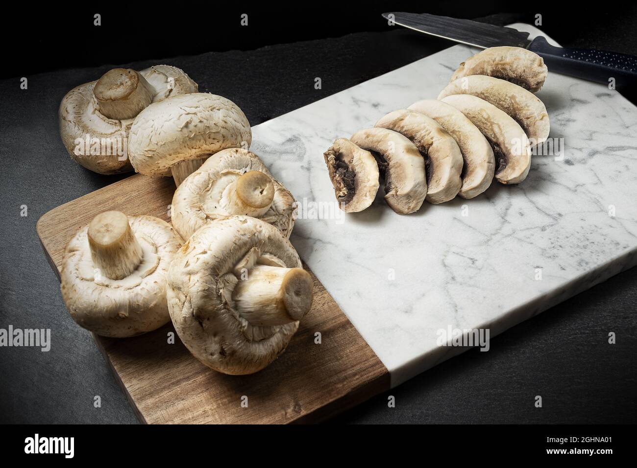 Closeup view of sliced up champignon mushrooms and whole mushrooms on a wooden board Stock Photo