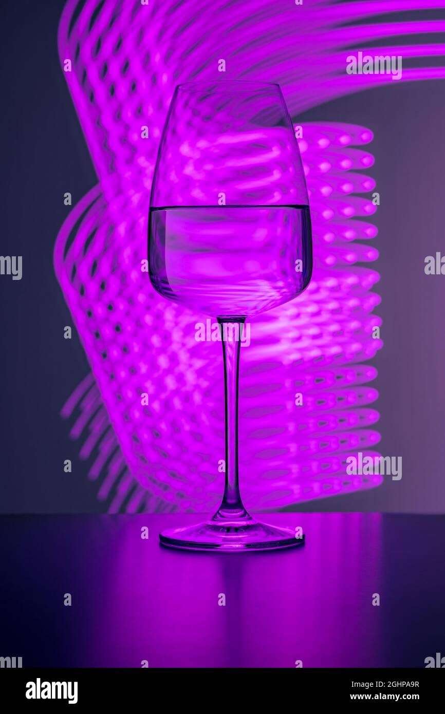 Elegant crystal glass filled with pure water on a purple background painted with colorful light. Light reflections and refractions, light streaks, par Stock Photo