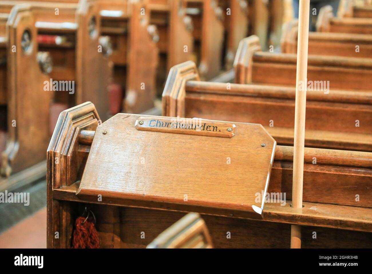 A wooden lectern with a sign on it saying 'churchwarden', and wooden pews in a church, England, UK Stock Photo