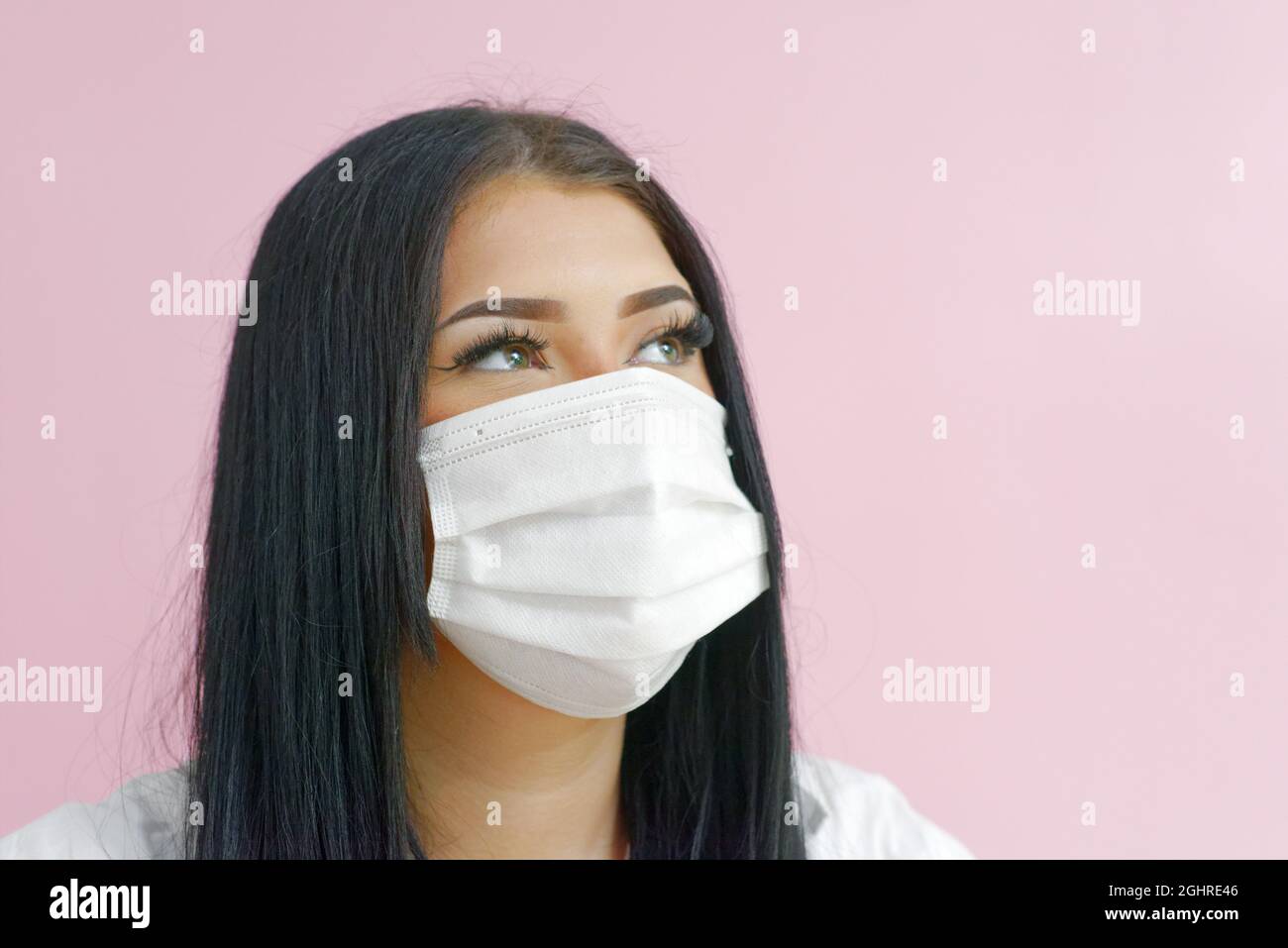 Girl with black hair and a mask on a pink background Stock Photo