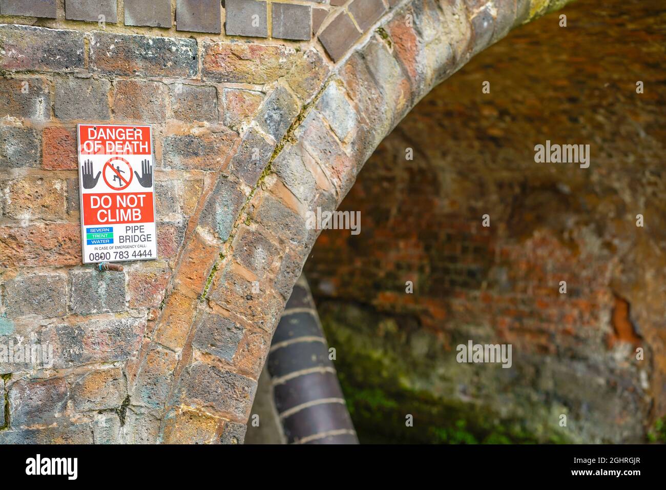 'Danger of Death, Do Not Climb' sign on the face of a brick pipe bridge over a UK canal, posted by Severn Trent Water. Stock Photo