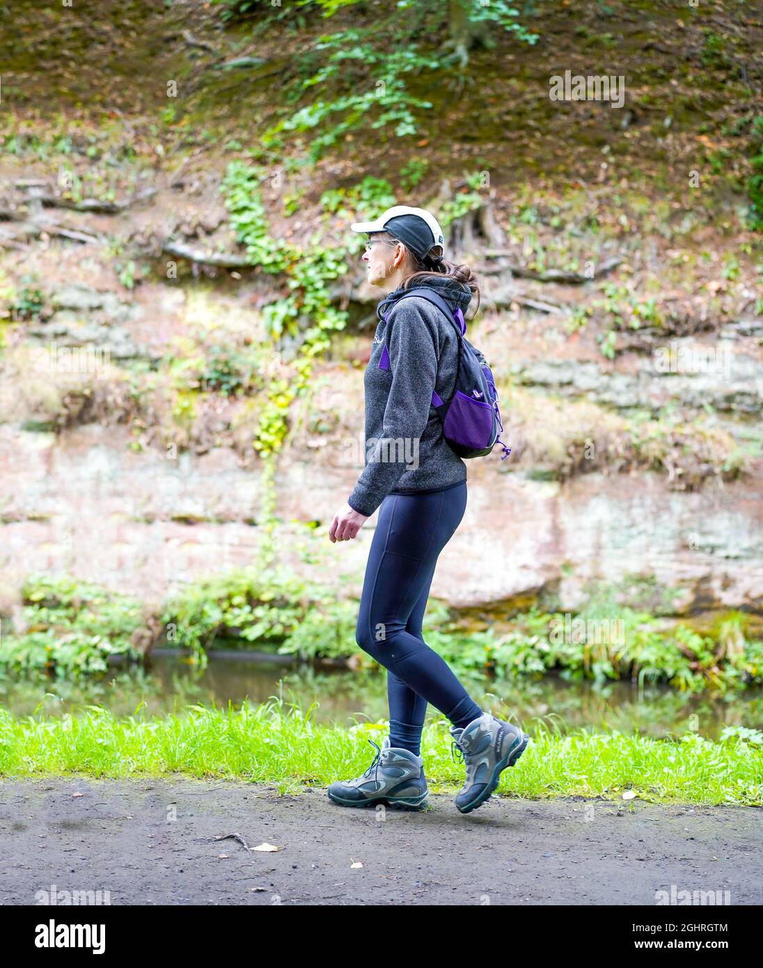 Isolated female, in sports cap and leggings, walking on rural towpath by UK countryside canal. Stock Photo