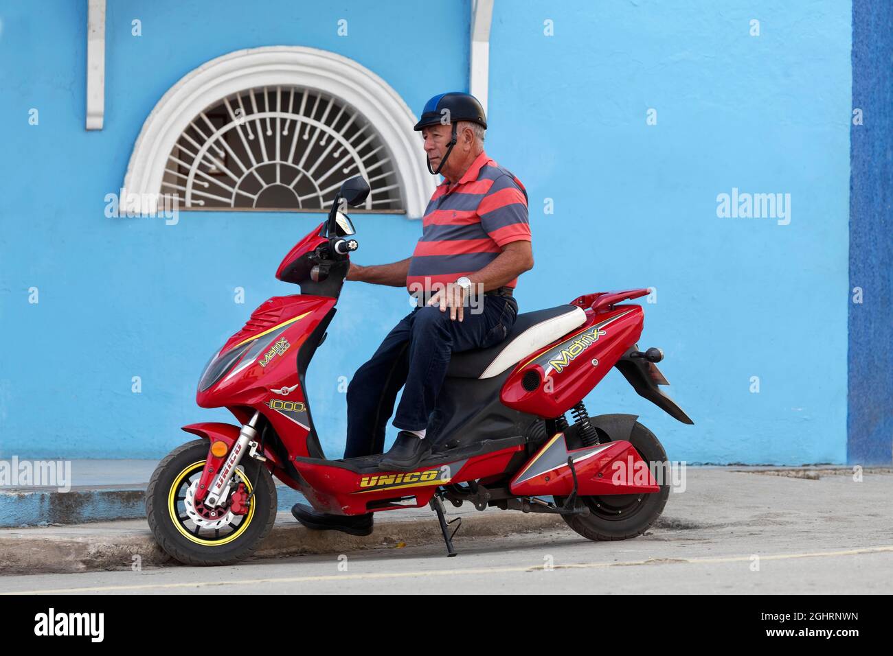 Man, Cuban on scooter, red, in front of house, blue, Sancti Spiritus, Central Cuba, Sancti Spiritus Province, Caribbean, Cuba Stock Photo