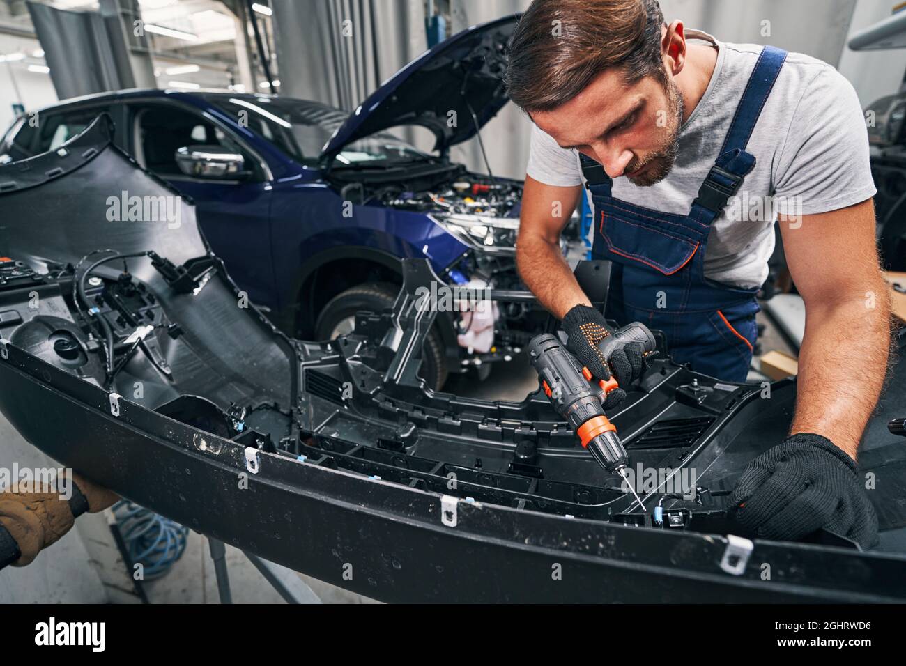 Car repair professional operating drill while working on engine Stock Photo