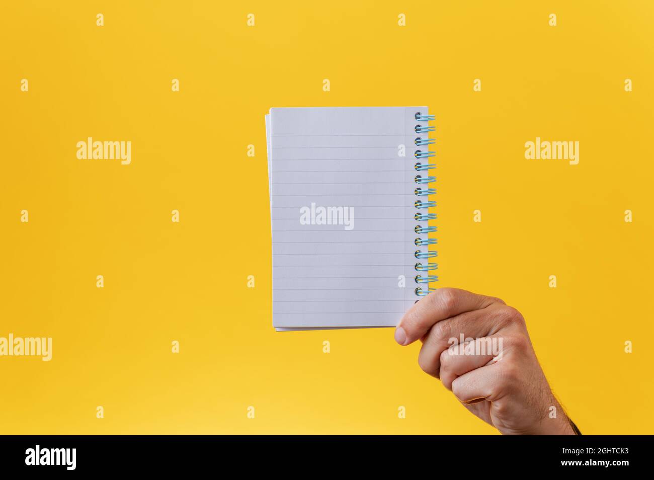 Male hand holding blank spiral notepad over yellow background. With copy space. Stock Photo