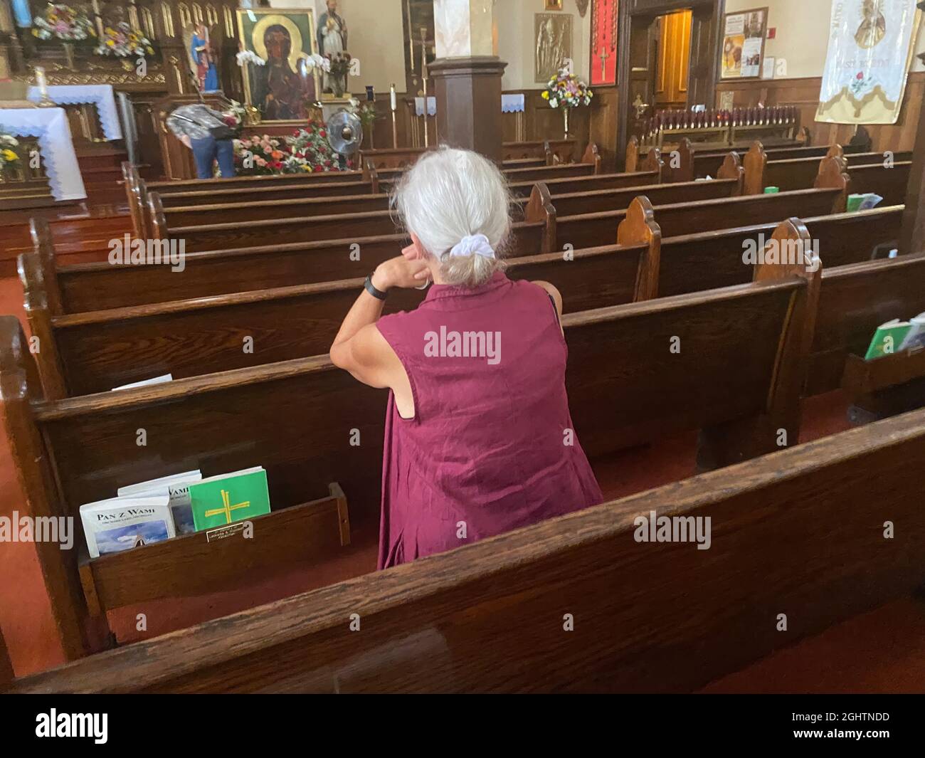 Woman deep in prayer at a Catholic Church in Sunset Park, Brooklyn, New York. Church is mostly empty due to the Covid-19 pandemic Stock Photo
