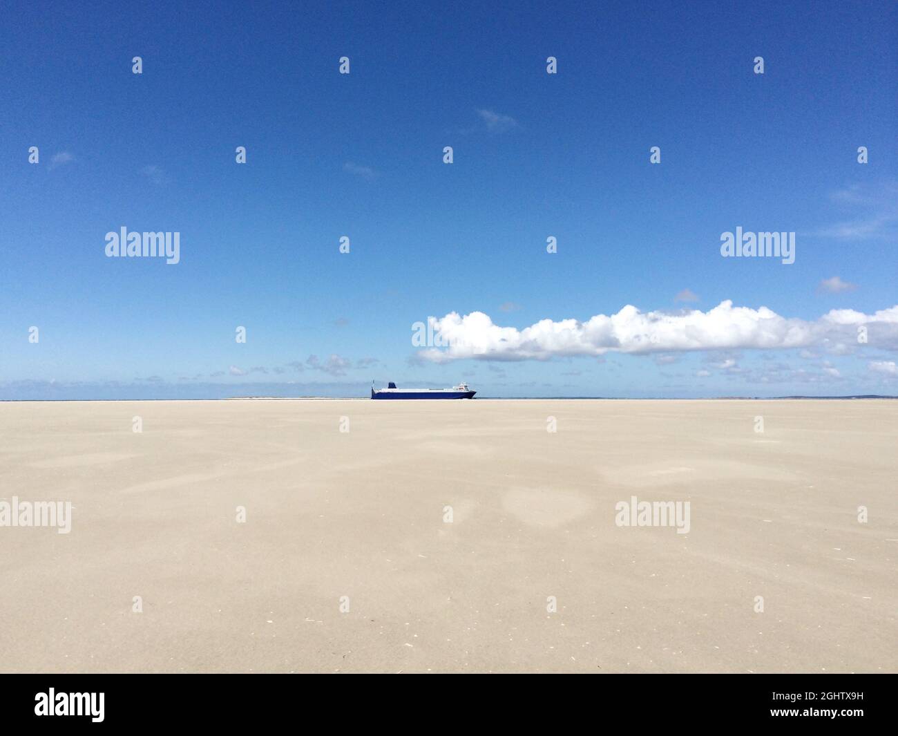 View from the beach of a ship sailing along coastline in the distance ...