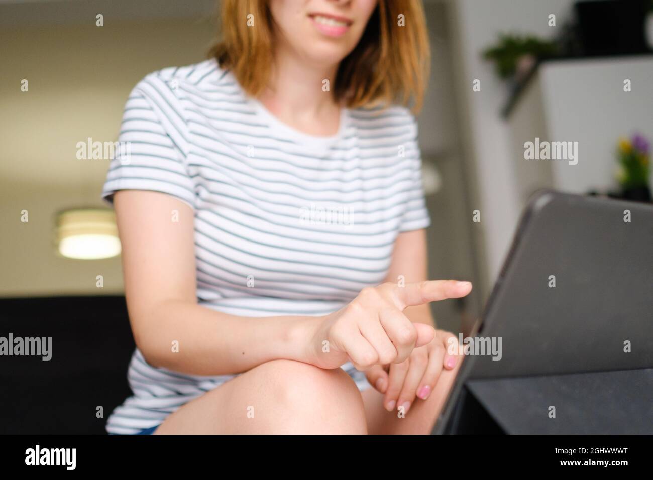 Casual woman uses tablet for inline conversation. Freelancer working online at modern living room.  Stock Photo