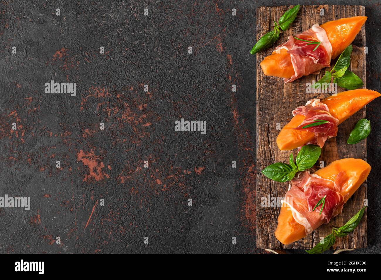 Melon cantaloupe slices with prosciutto ham and basil on black