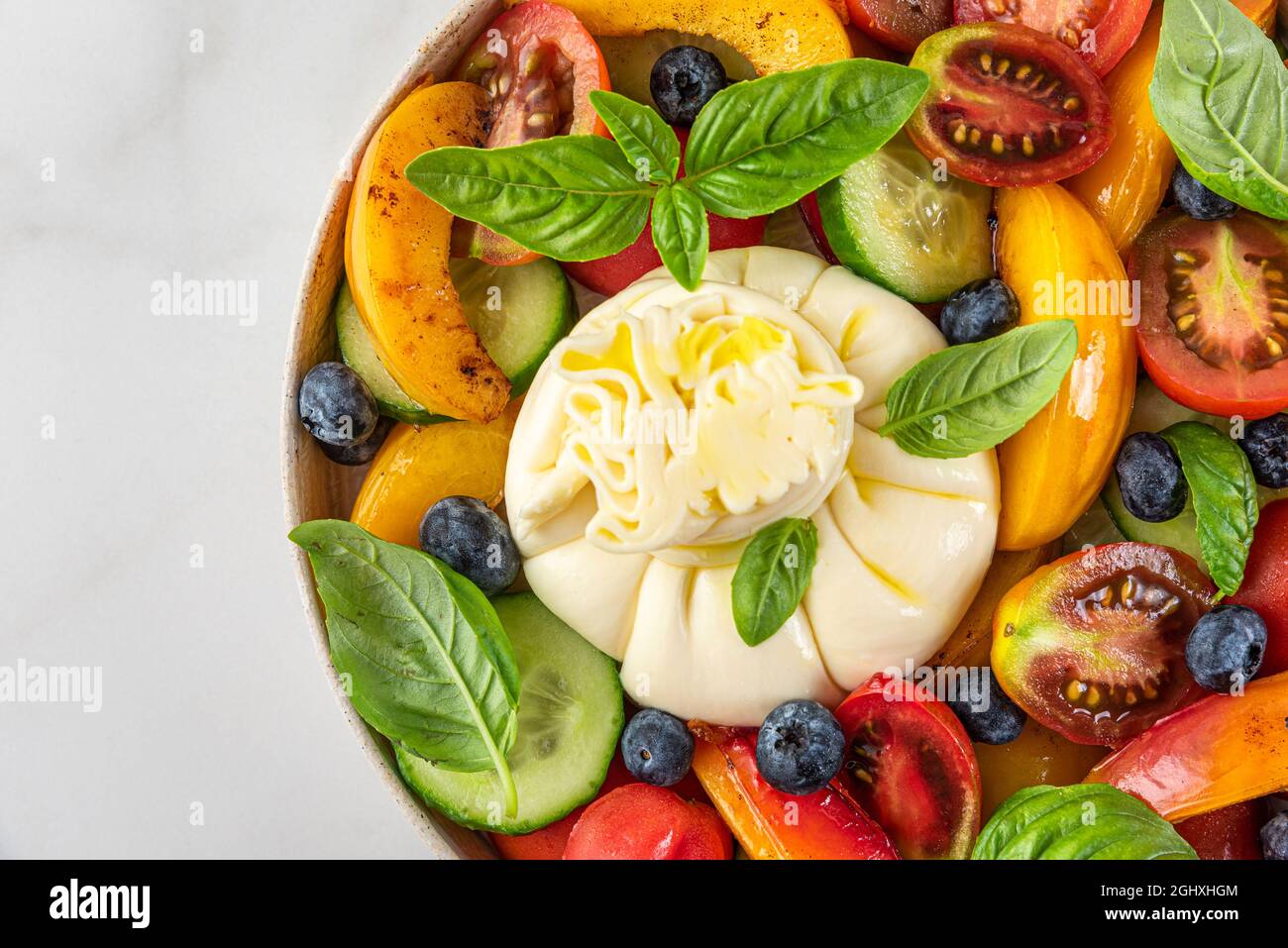 Fresh salad with grilled peaches, burrata cheese, blueberries and vegetables on a plate on white background. Top view. Healthy diet summer food concep Stock Photo