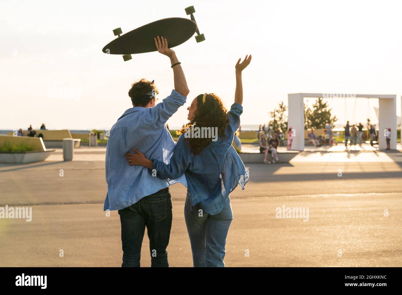Happy couple enjoy sunset embrace with arms raised hold longboard. Happiness and freedom concept Stock Photo