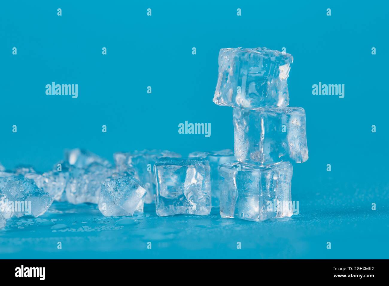 Lots of ice cubes and shards of ice on a blue background. three ice cubes stand one on the other on a blue background. Stock Photo
