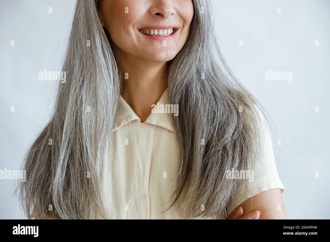 Middle aged woman with long silver hair smiles on light grey background Stock Photo