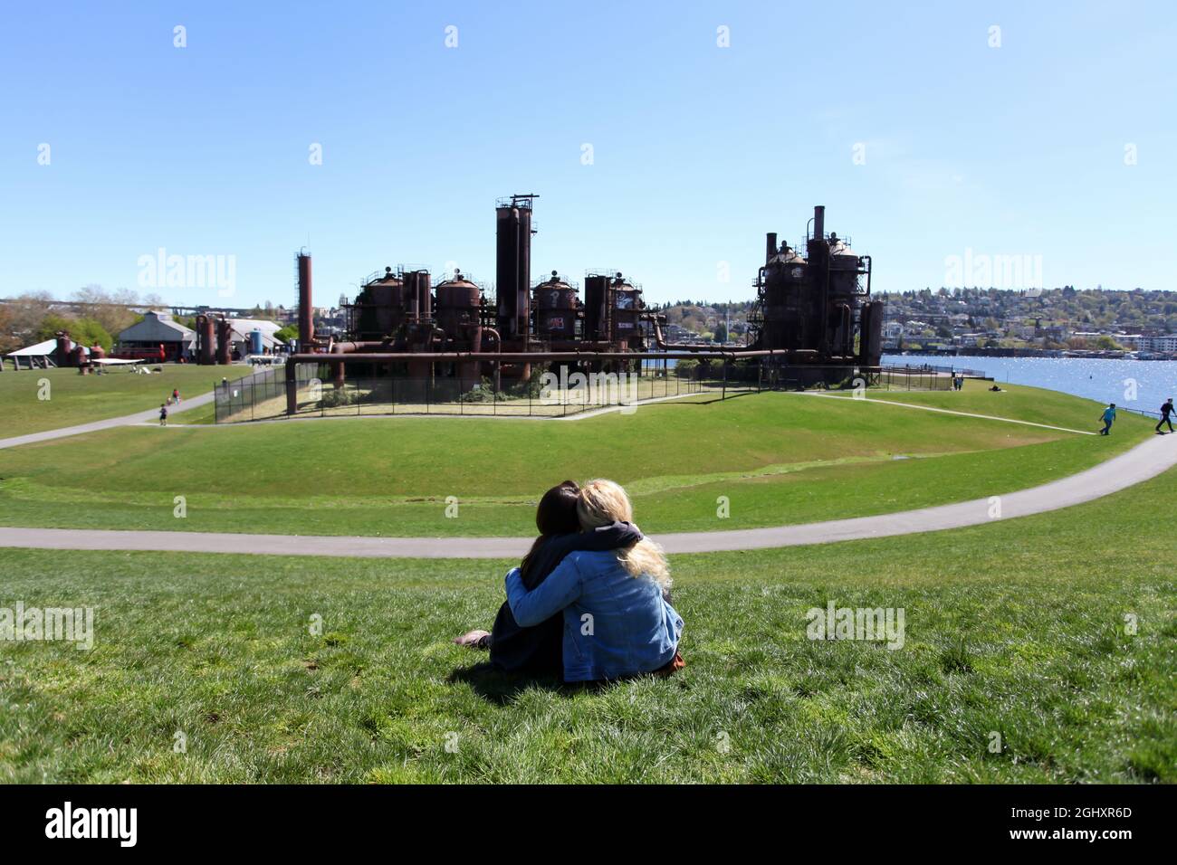 Two women sitting on the grass hill and hugging in front of Gas Works Park in Seattle. Stock Photo
