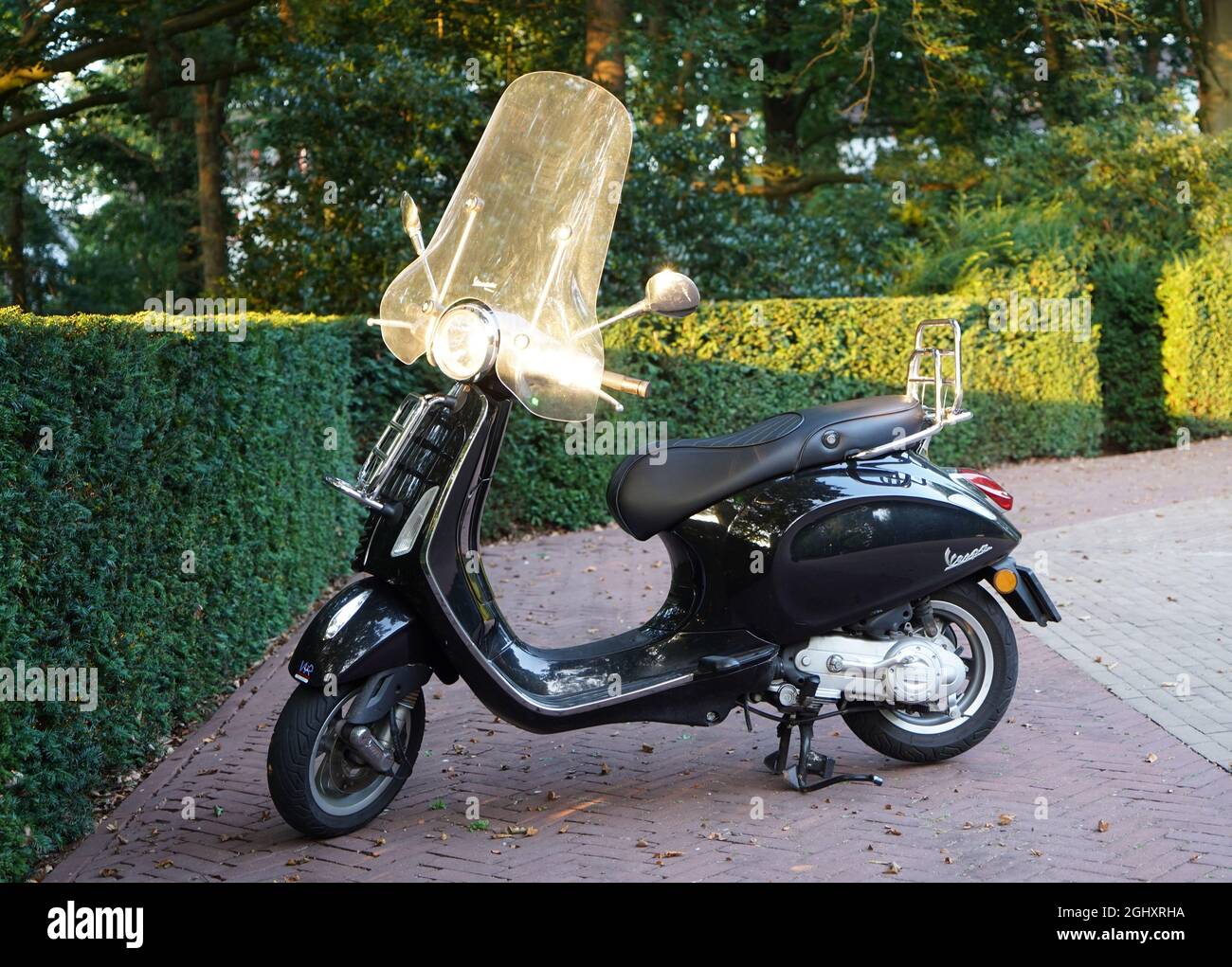 Amersfoort, the Netherlands - September 3 2021. A black Vespa scooter with windscreen parked on an empty parking place with green hedges Stock Photo