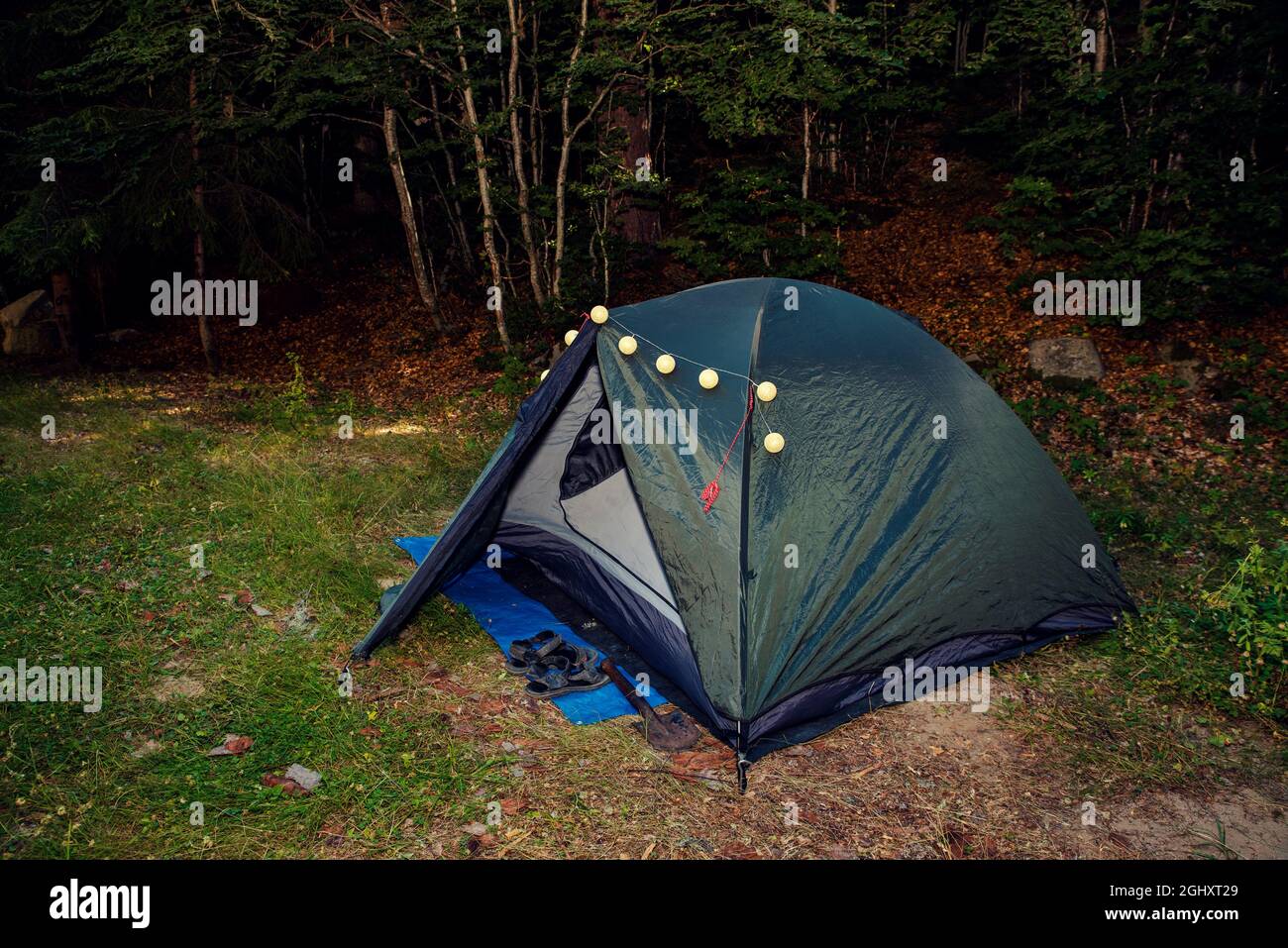 Green tent with decoration lights in the woods with sandals and shovel in  front the entrance. Summertime camping Stock Photo - Alamy