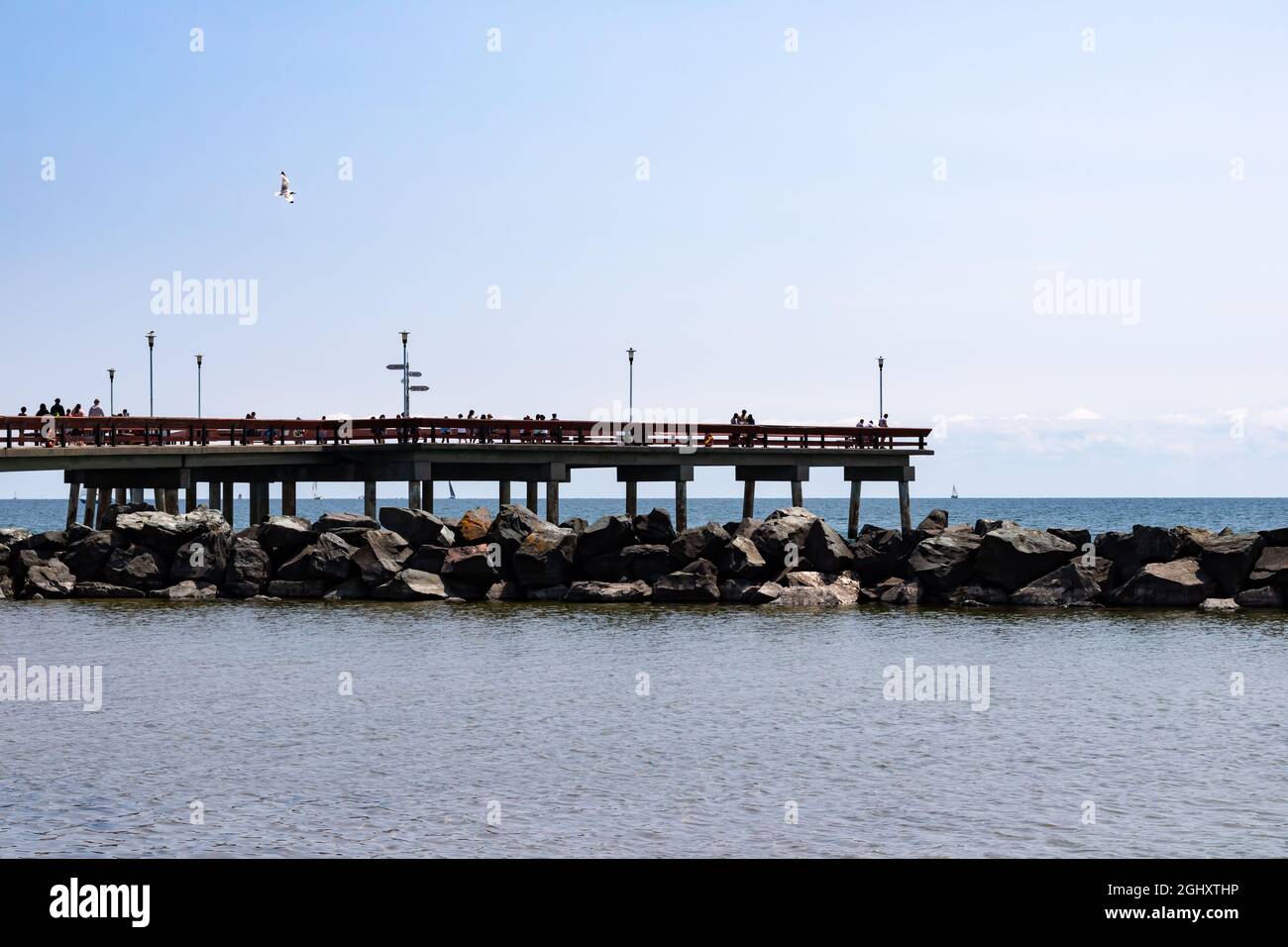 Toronto, Ontario, Canada - July 31 2021: People on a concrete and wooden pier that overlooks Lake Ontario on the Toronto Islands. Above rocks. Stock Photo