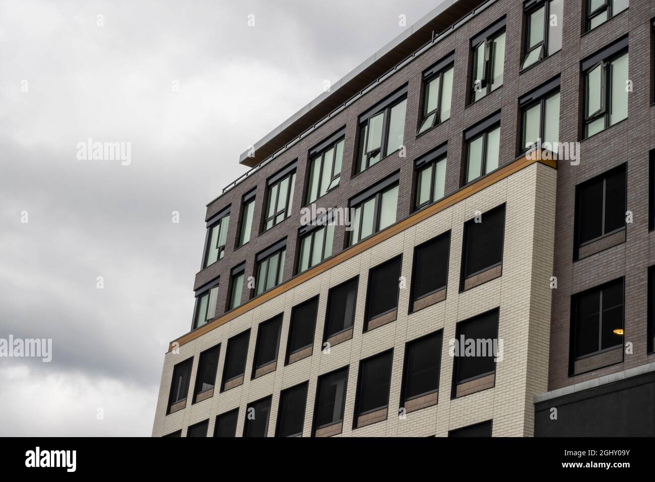 Angled view of a large, window covered apartment building corner against a blue, cloud filled sky Stock Photo