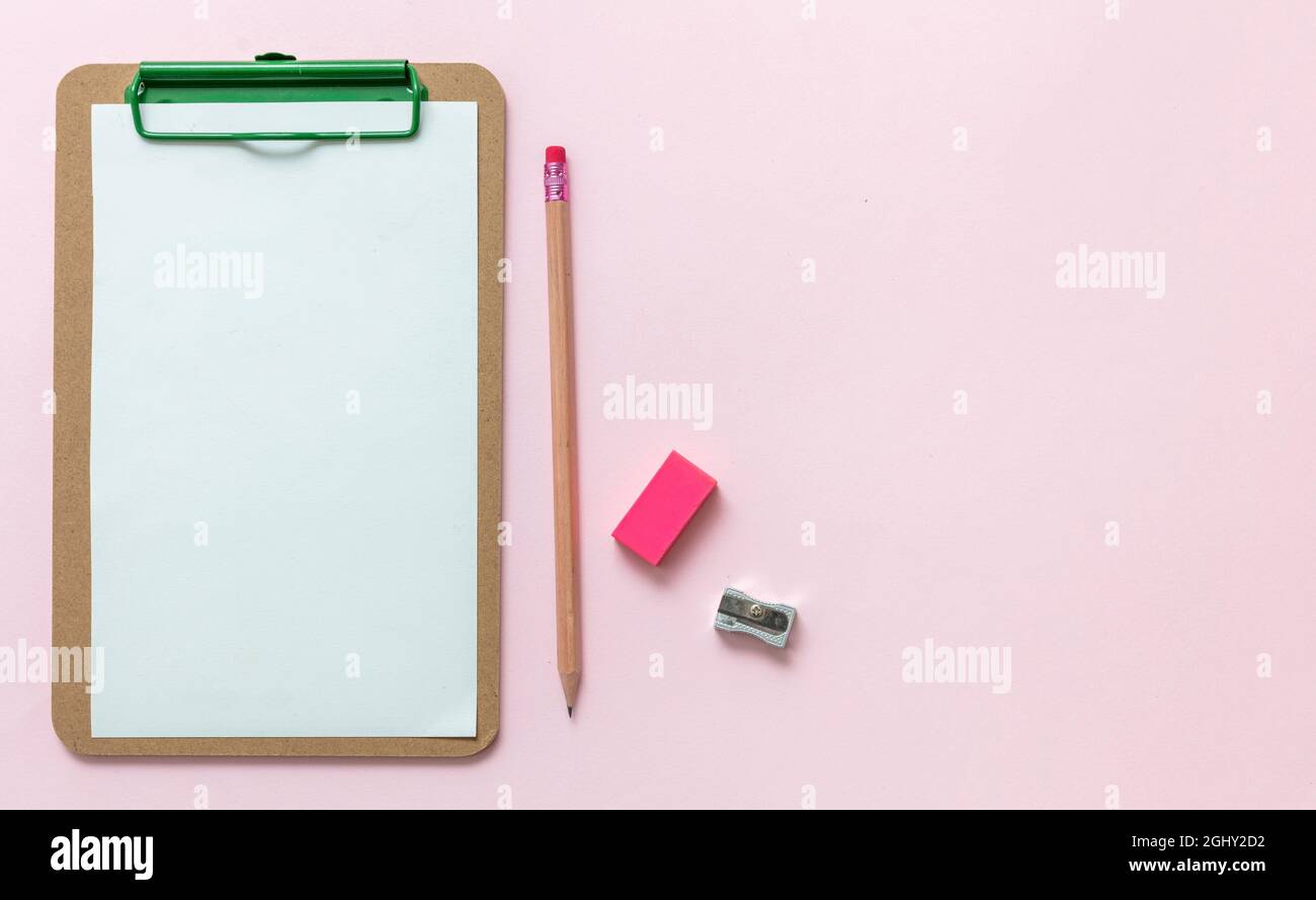 School supplies, student desk top view, Blank paper clipboard, pencil eraser and sharpener on pink background, copy space, template. Stock Photo