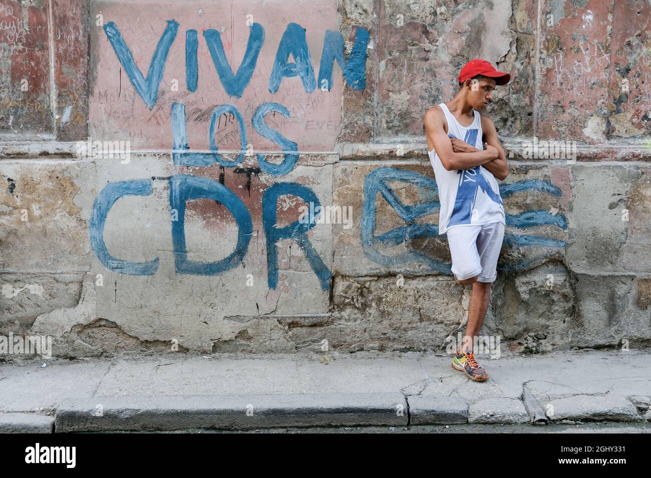 A man stands next to graffiti that reads 'Vivan Los CDR' in Havana, Cuba. Stock Photo