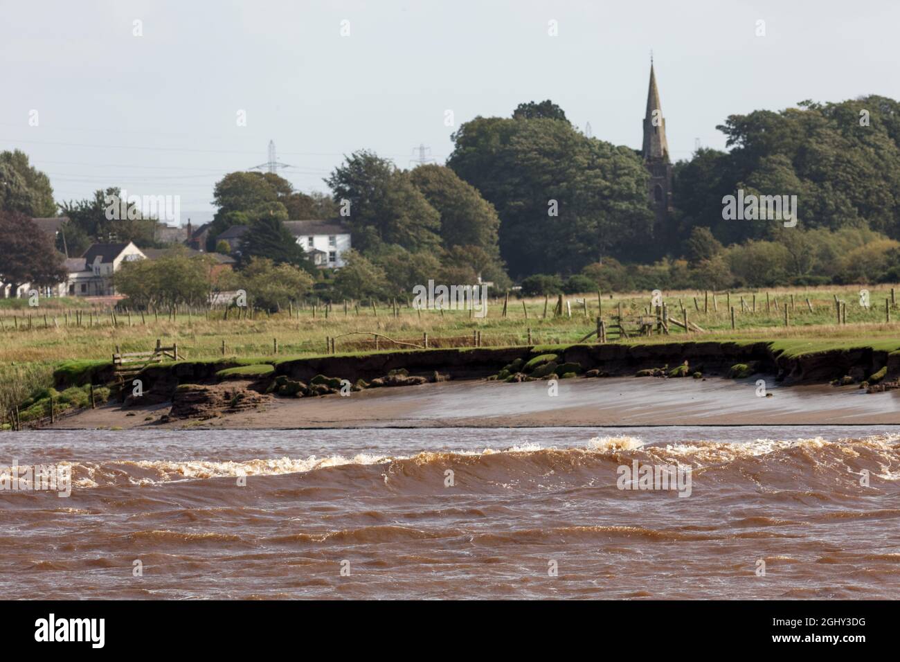 The Solway Bore travelling along the channel of the River Eden with Rockcliffe village in the background Stock Photo
