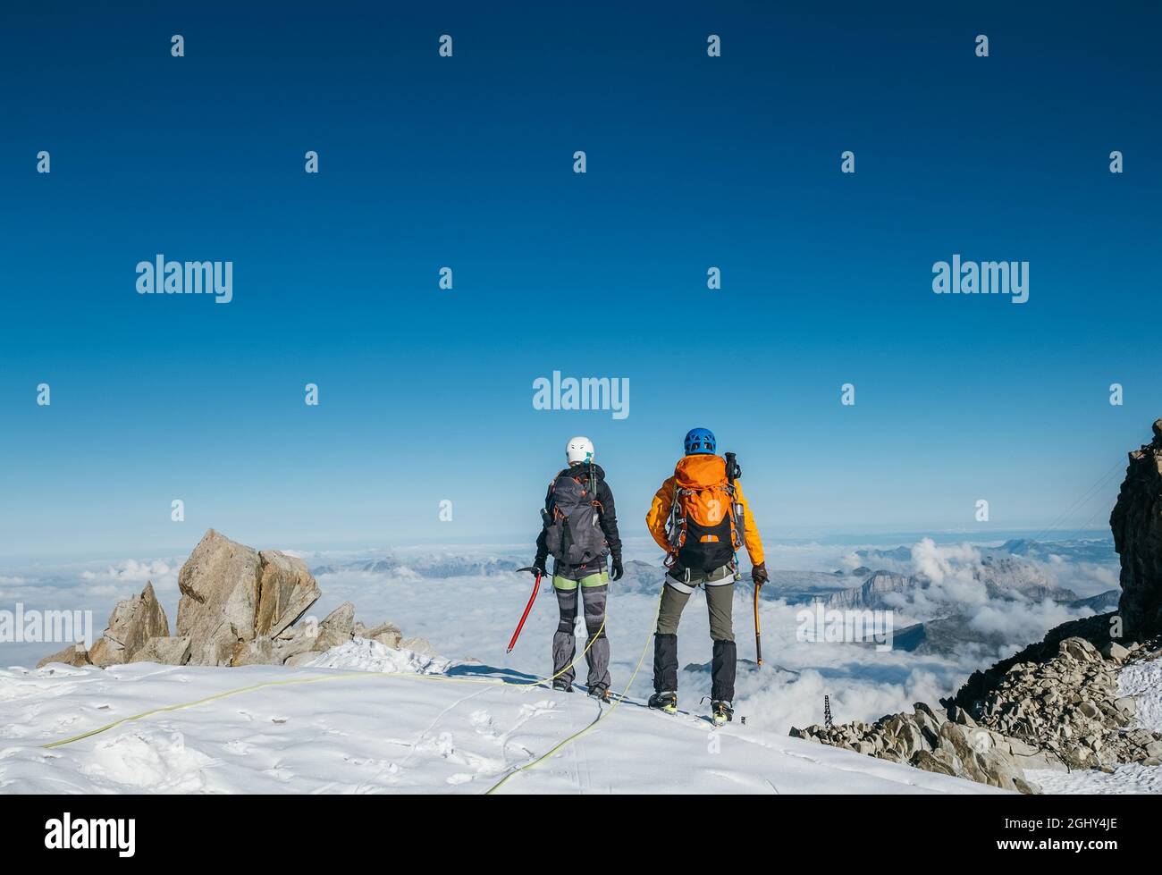 Couple connected team rope  with climbing harness dressed mountaineering clothes with backpacks and ice axes enjoying views ascending Mont Blanc (Mont Stock Photo