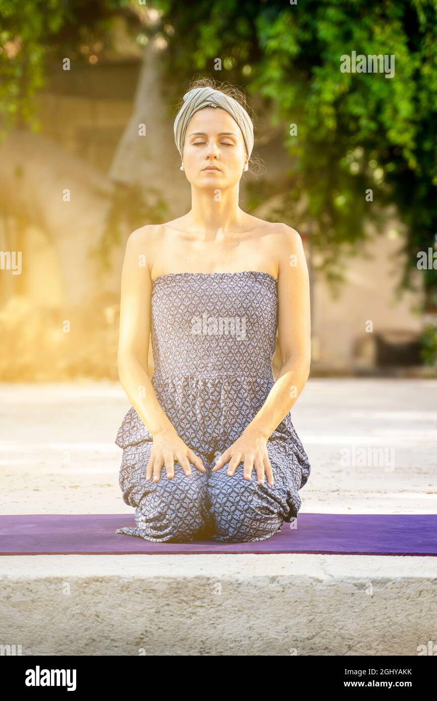 beautiful girl kneeling with closed eyes practicing meditation outdoors Stock Photo